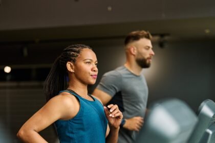 Portrait of a young black woman and white man exercising in a gym, running using  thereadmill machine equipment, healthy lifestyle and cardio exercise at fitness club concepts